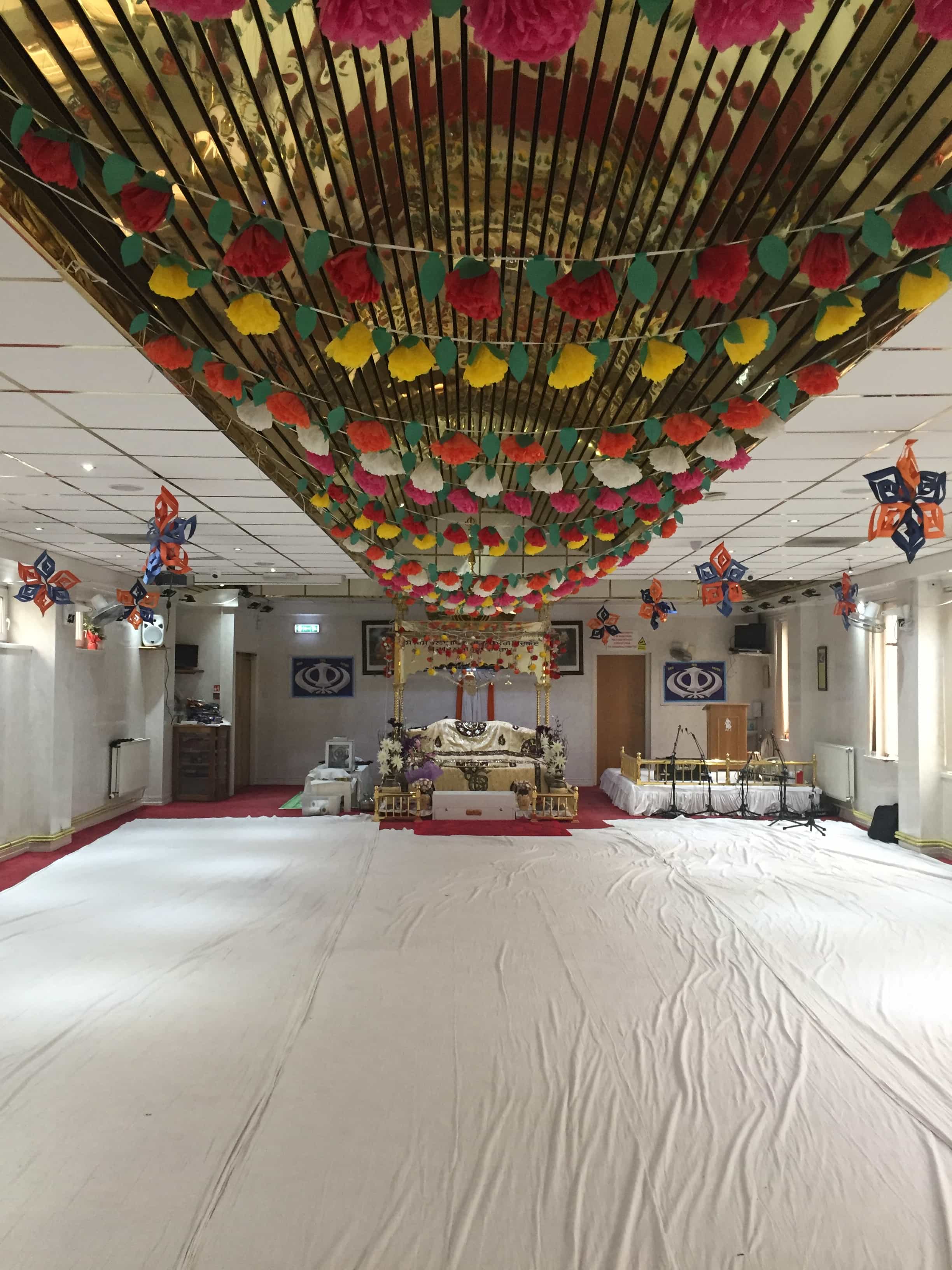 Decorated Sikh Gurudwara prayer hall &mdash; flower garlands and gold ceiling, fitted by Opus AV